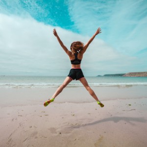 Young woman doing star jumps on the beach
